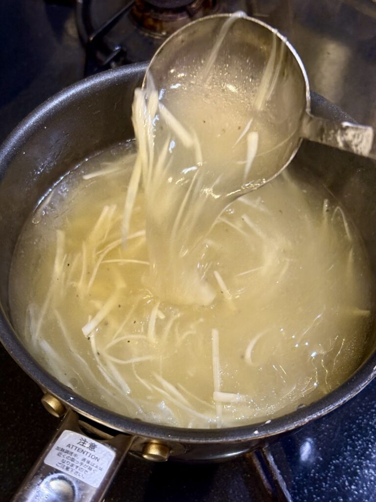 細切りのホワイトアスパラを入れたマグロテールスープに軽くとろみをつけている様子