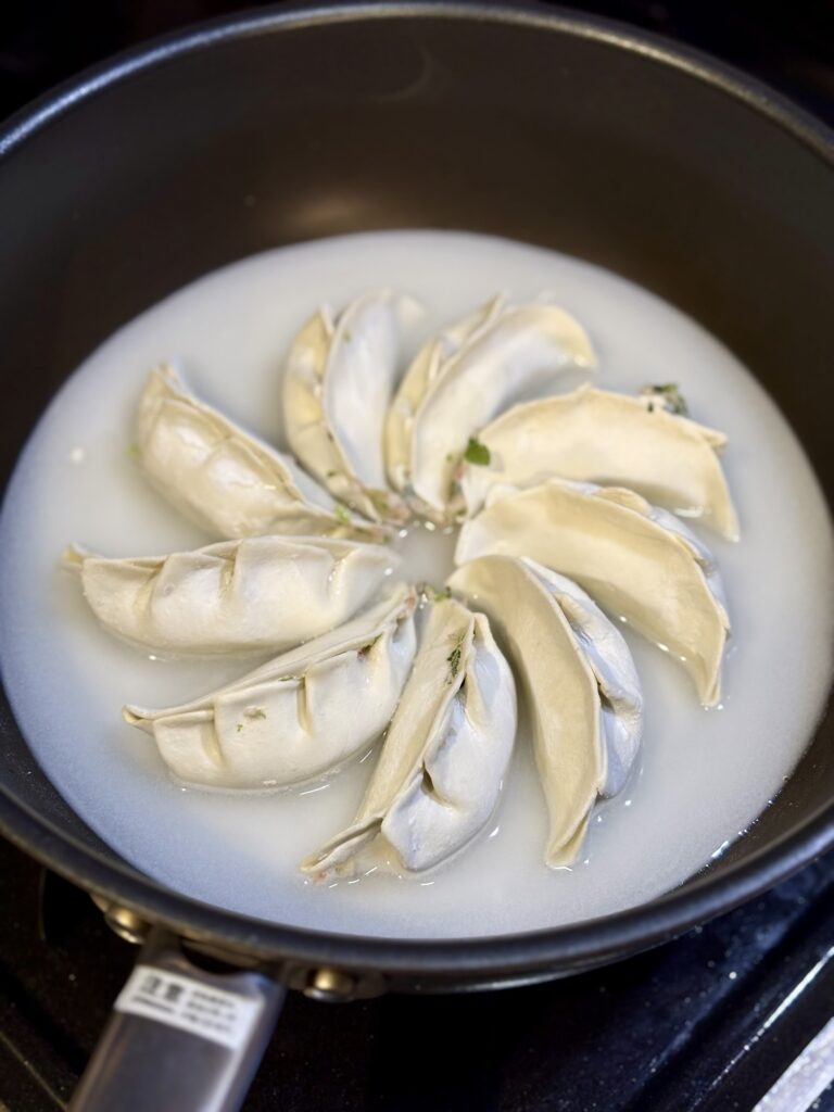 フライパンに餃子を円形に並べ、水溶き粉を注いで羽根つき餃子を焼く前の工程写真