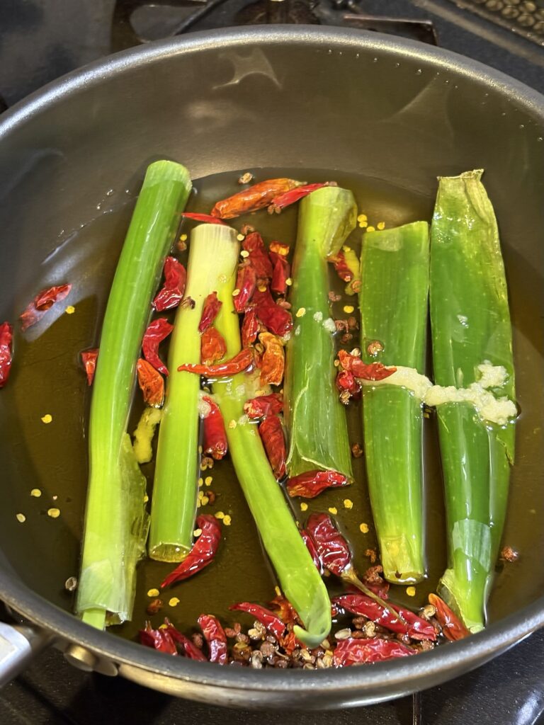 フライパンに長ねぎ、唐辛子、花椒、にんにくを入れて自家製辣油の香味油を作っている写真