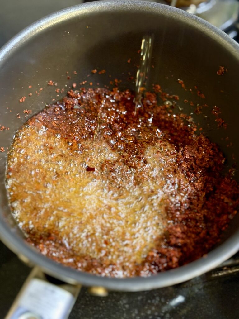 熱い香味油を唐辛子粉に注いで自家製辣油を作っている写真