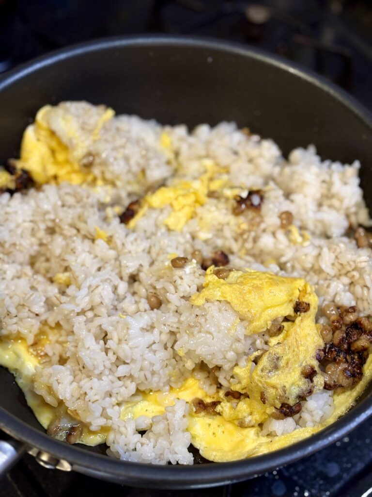 納豆と卵を炒めたところにごはんを加えてチャーハンにしている様子