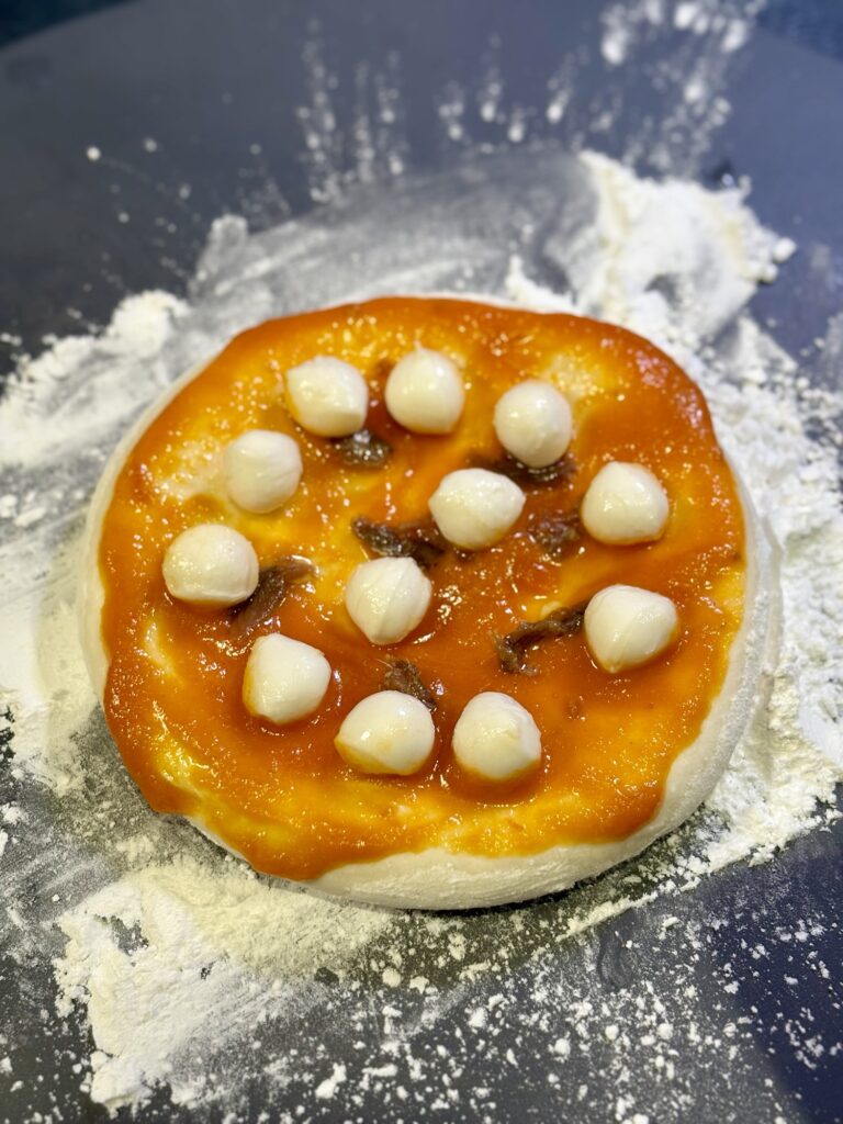 くんのトマトソースを塗ったピザ生地にパールモッツァレラとアンチョビをのせる