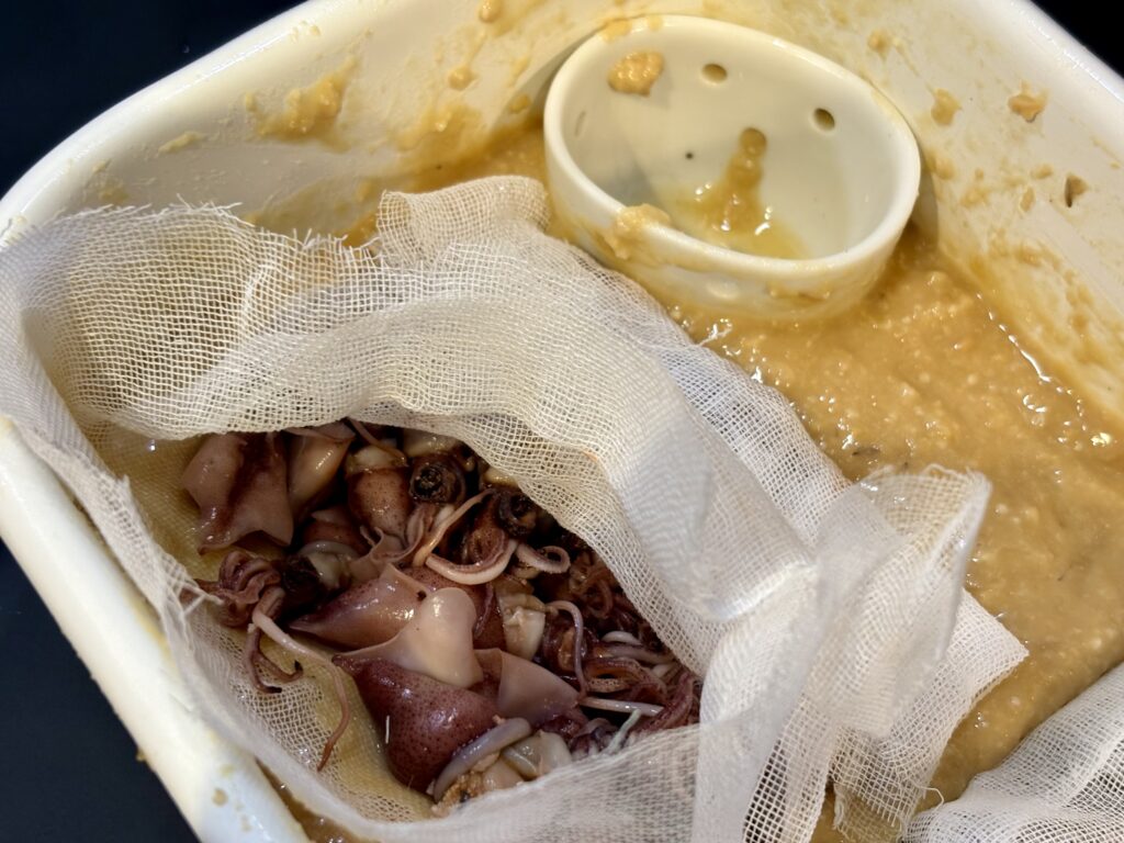 味噌床の容器でホタルイカをガーゼに包んで西京漬けにしている様子
