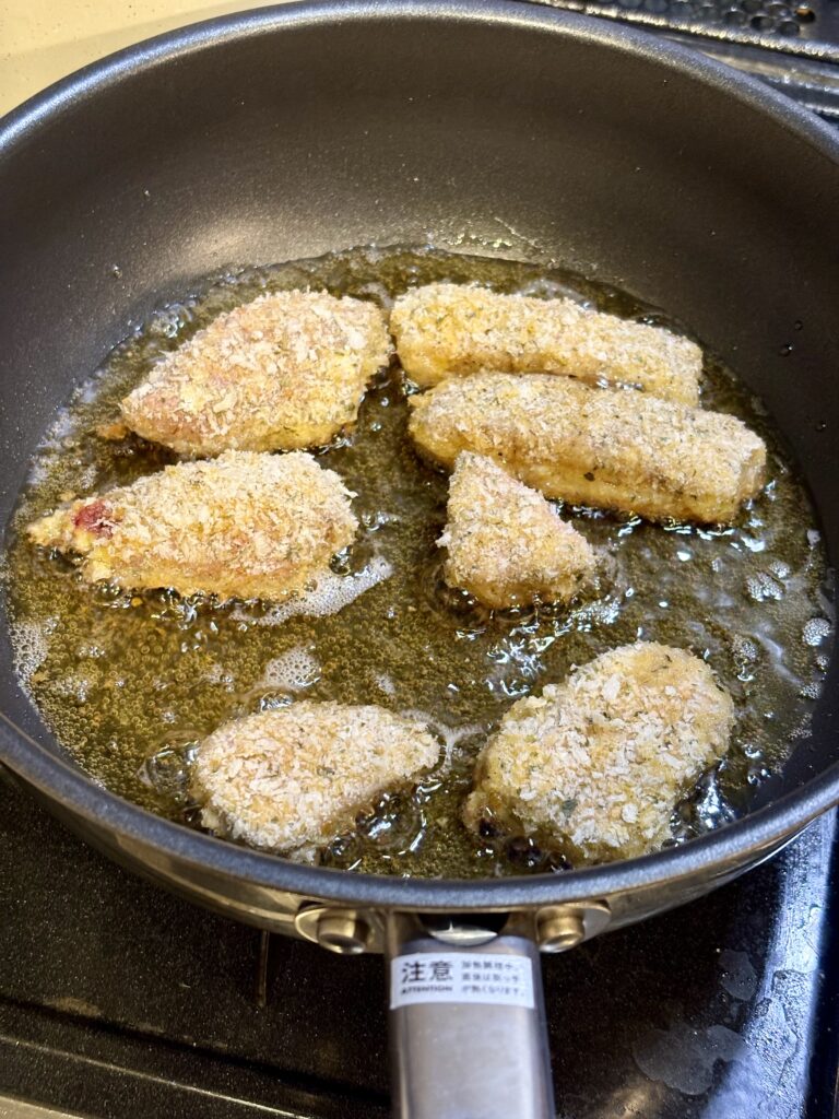 低温調理後の肉に衣を付け、フライパンで揚げ焼きしている様子。カツレツの加熱初期段階
