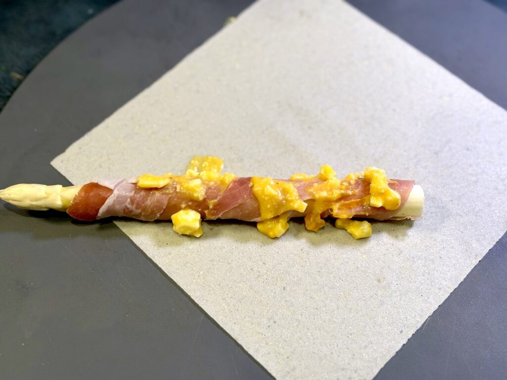 ホワイトアスパラに卵ソースを塗り春巻きの皮で巻いている写真