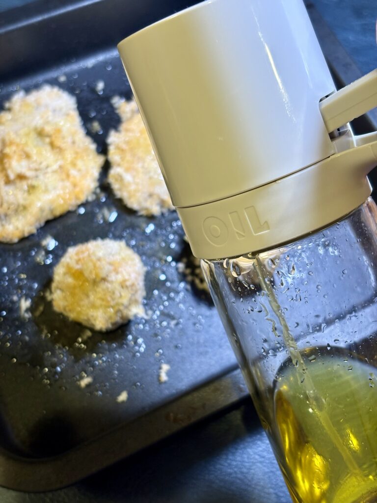衣をつけた牡蠣フライとミートボールフライにオイルスプレーでオリーブオイルをかける写真