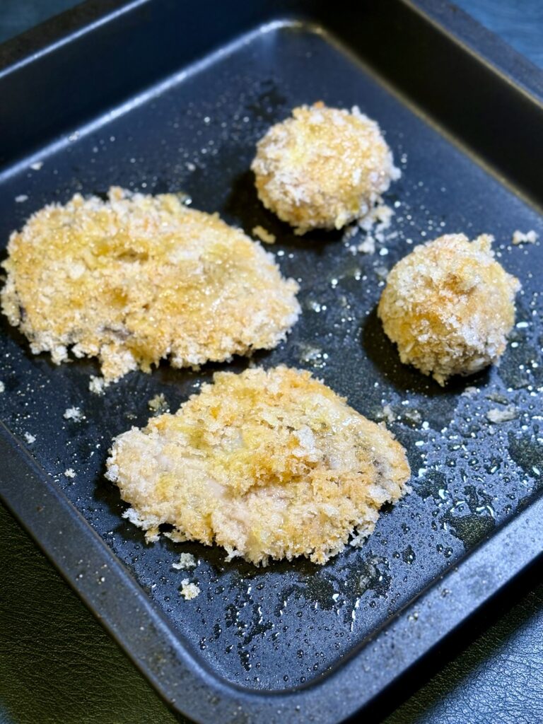オリーブオイルをかけた牡蠣フライとミートボールフライを天板に並べた写真