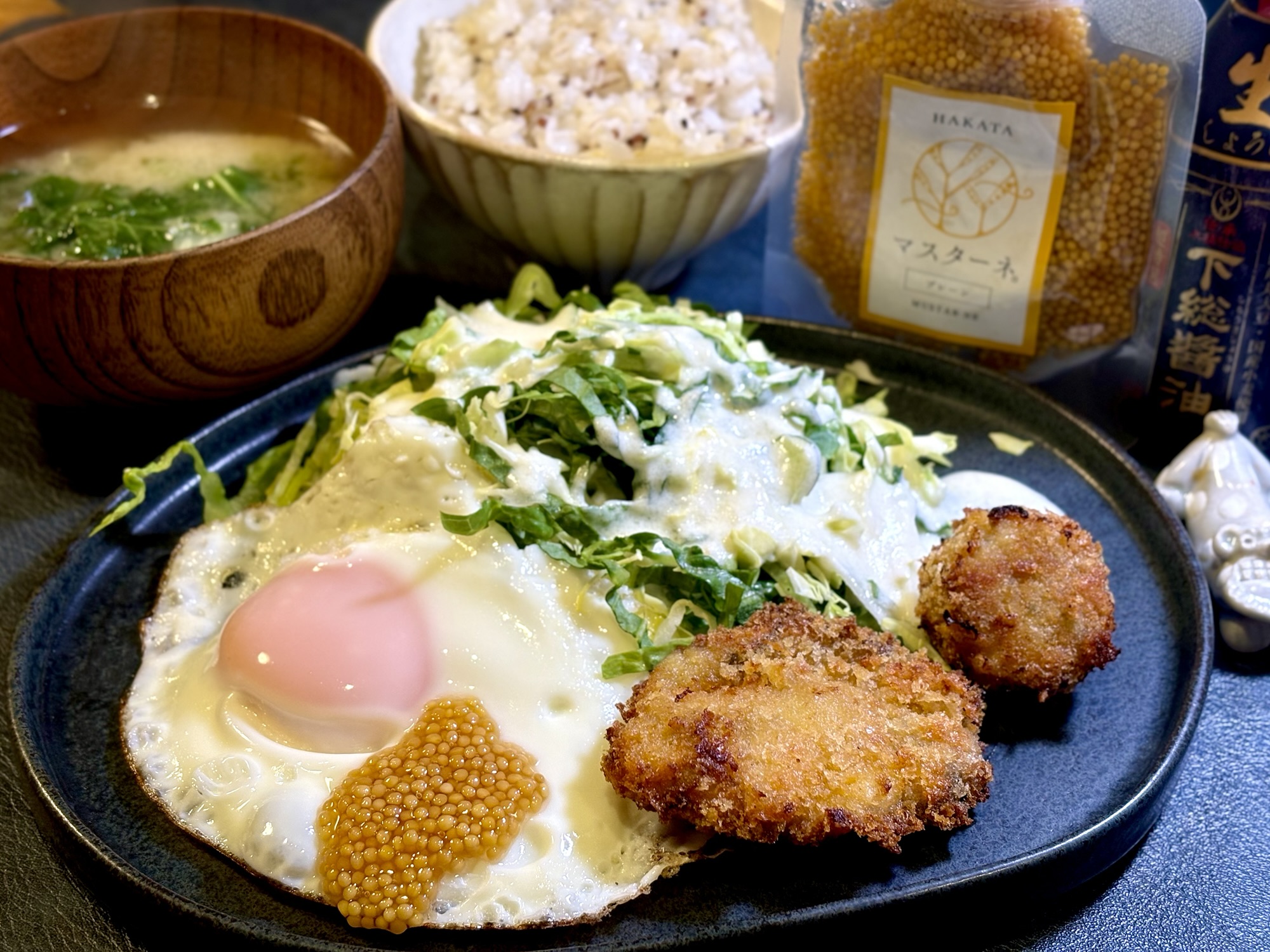 牡蠣フライとミートボールフライ、目玉焼き、春キャベツと新玉ねぎのサラダ、ごはん、味噌汁を添えた朝ごはんプレートの写真