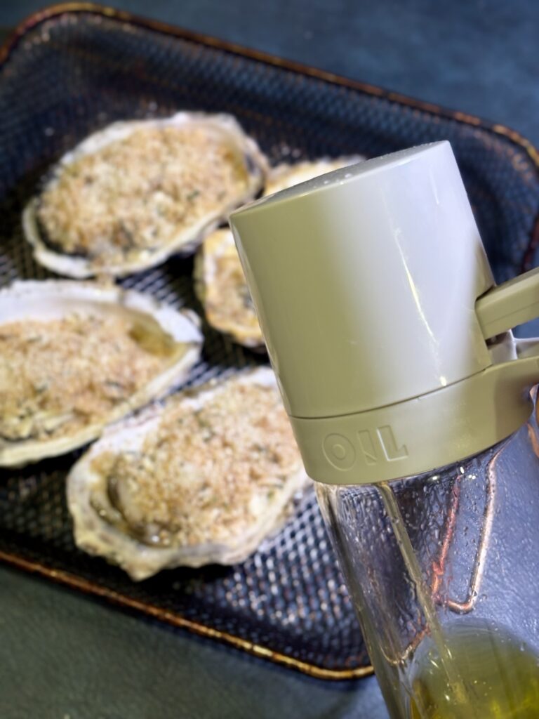 香草パン粉をのせた牡蠣にオイルスプレーでオリーブオイルをかける写真
