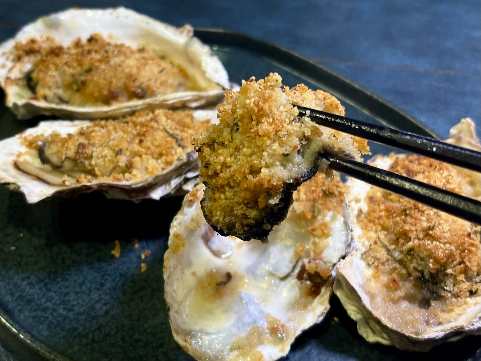 箸で持ち上げた牡蠣の香草パン粉焼きの写真