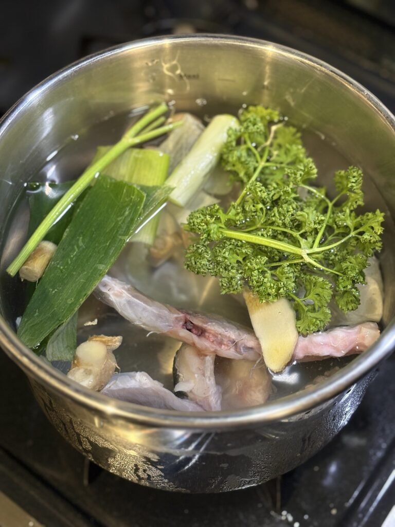 魚の骨と長ねぎ、パセリ、生姜、にんにく、酒、水で魚出汁を仕込む様子
