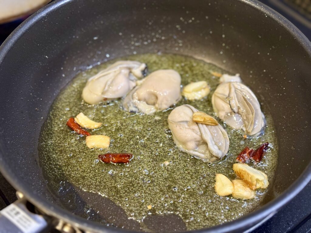 牡蠣をにんにくと唐辛子入りのオリーブオイルで炒めている様子