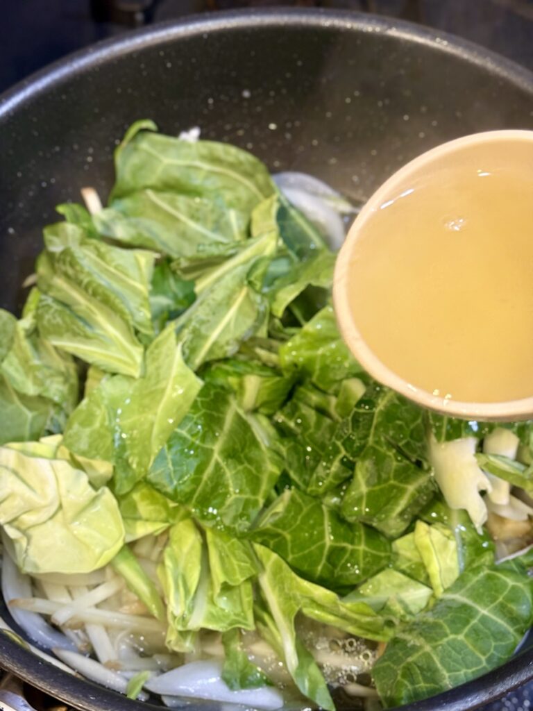 牡蠣と春野菜のフライパンに黄金スープを注いでいる様子