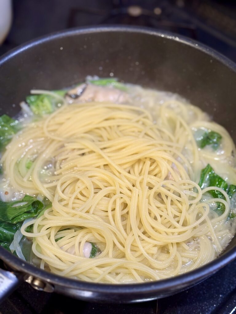 黄金スープと牡蠣、春野菜のソースにパスタを加えている様子