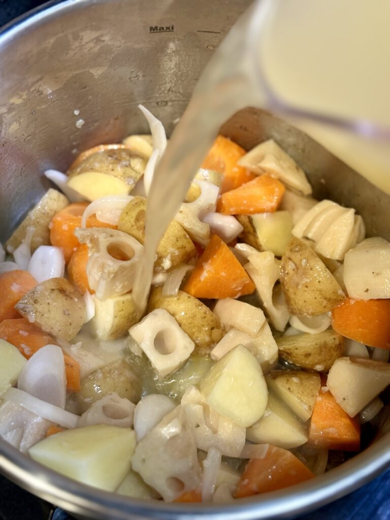 炒めた根菜の鍋に魚出汁を注いでいる様子
