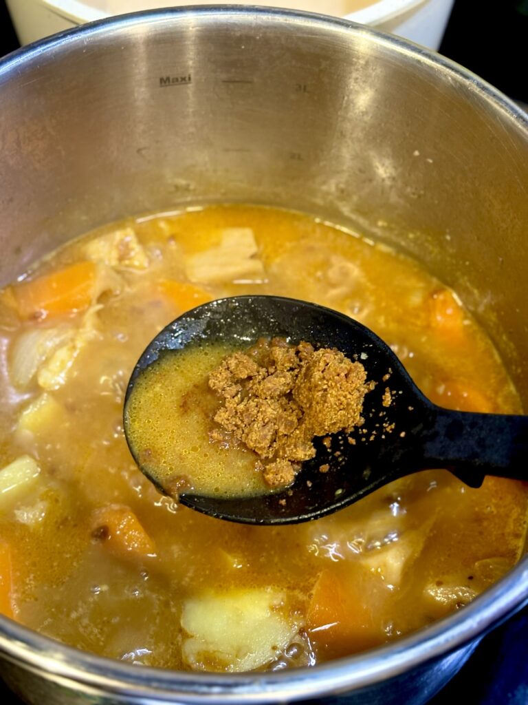 魚出汁と根菜の鍋に無印のカレールーを加える様子